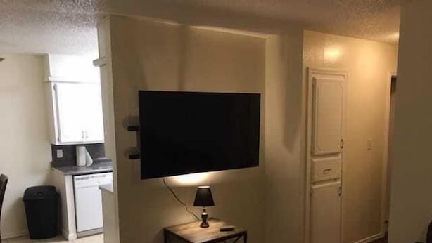 Un salon avec un téléviseur à écran plat fixé au mur, une petite table avec une lampe et une porte sur le côté droit.