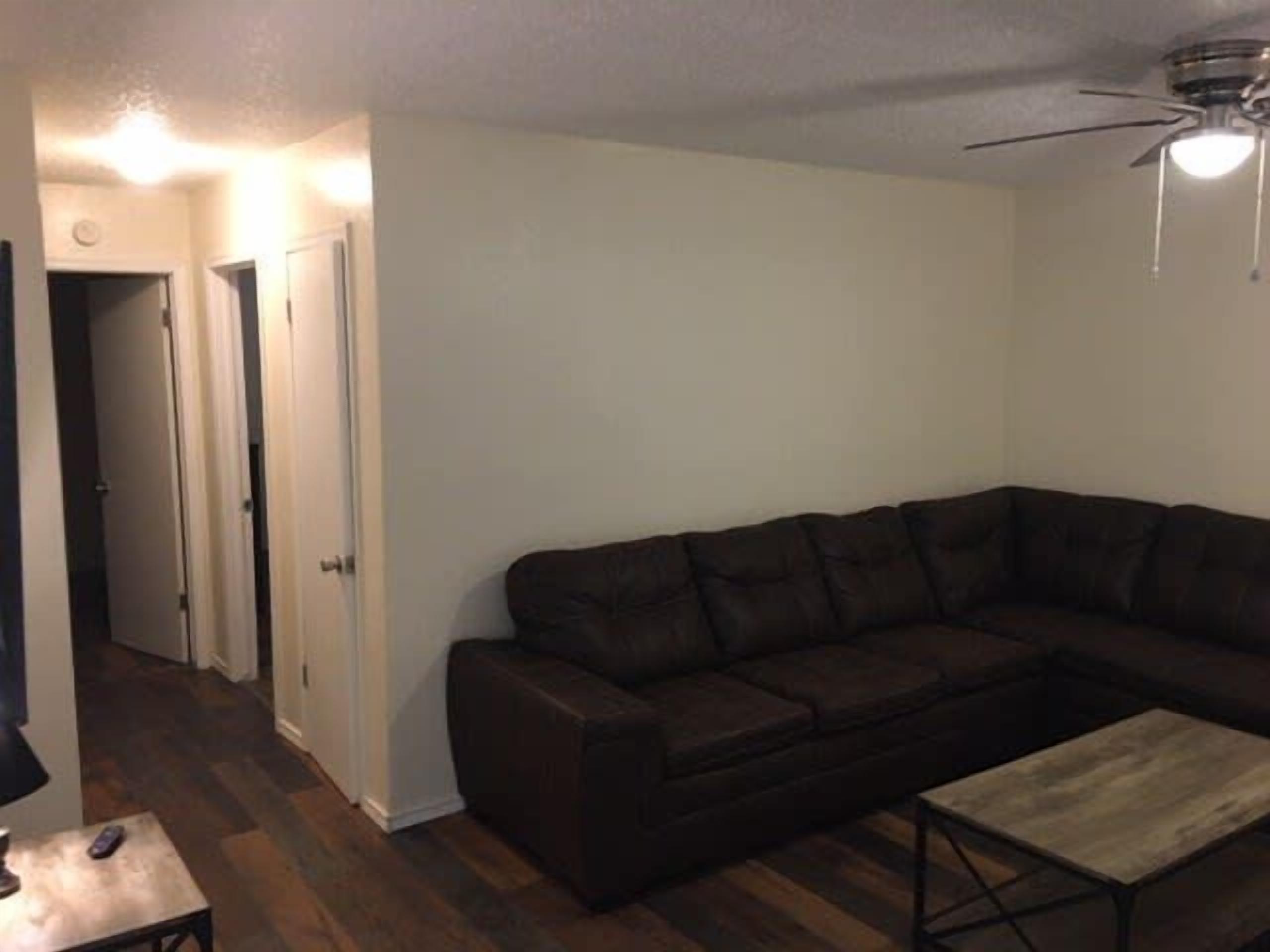 A living room with a dark brown sectional sofa, a wooden coffee table, and a ceiling fan.