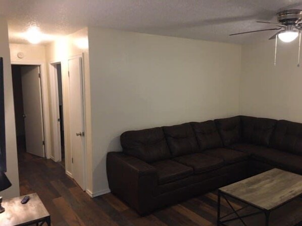 A living room with a dark brown sectional sofa, a wooden coffee table, and a ceiling fan.