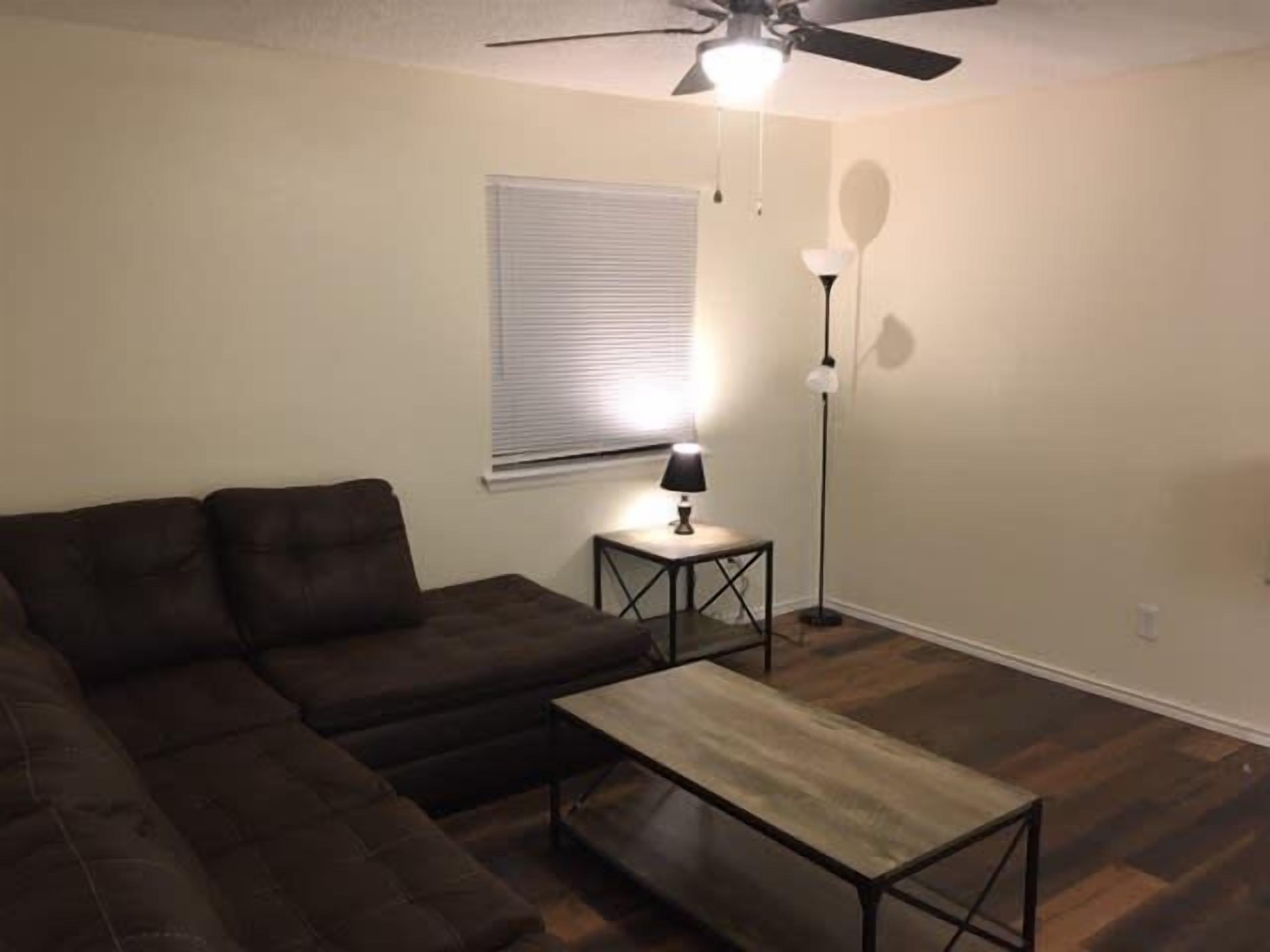 A living room with a sectional sofa, a coffee table, a floor lamp, and a ceiling fan.