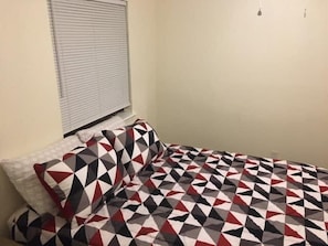 A bedroom with a bed, pillows, and a window with blinds.