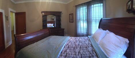 A bedroom with a wooden bed, a dresser, a mirror, and a window with blinds.