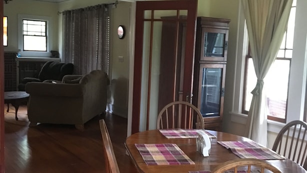 Un coin repas avec une table en bois, des chaises et un lustre. On aperçoit un canapé et un meuble en arrière-plan.