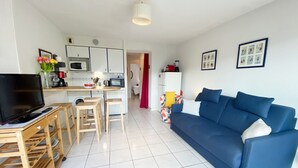 Een compacte woonruimte met kitchenette, een blauwe bank, een televisie en een eethoek met krukjes.