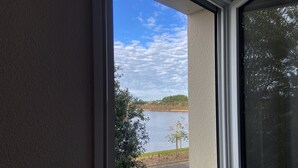 Uitzicht vanuit een raam op een meer met bomen en een heldere lucht.