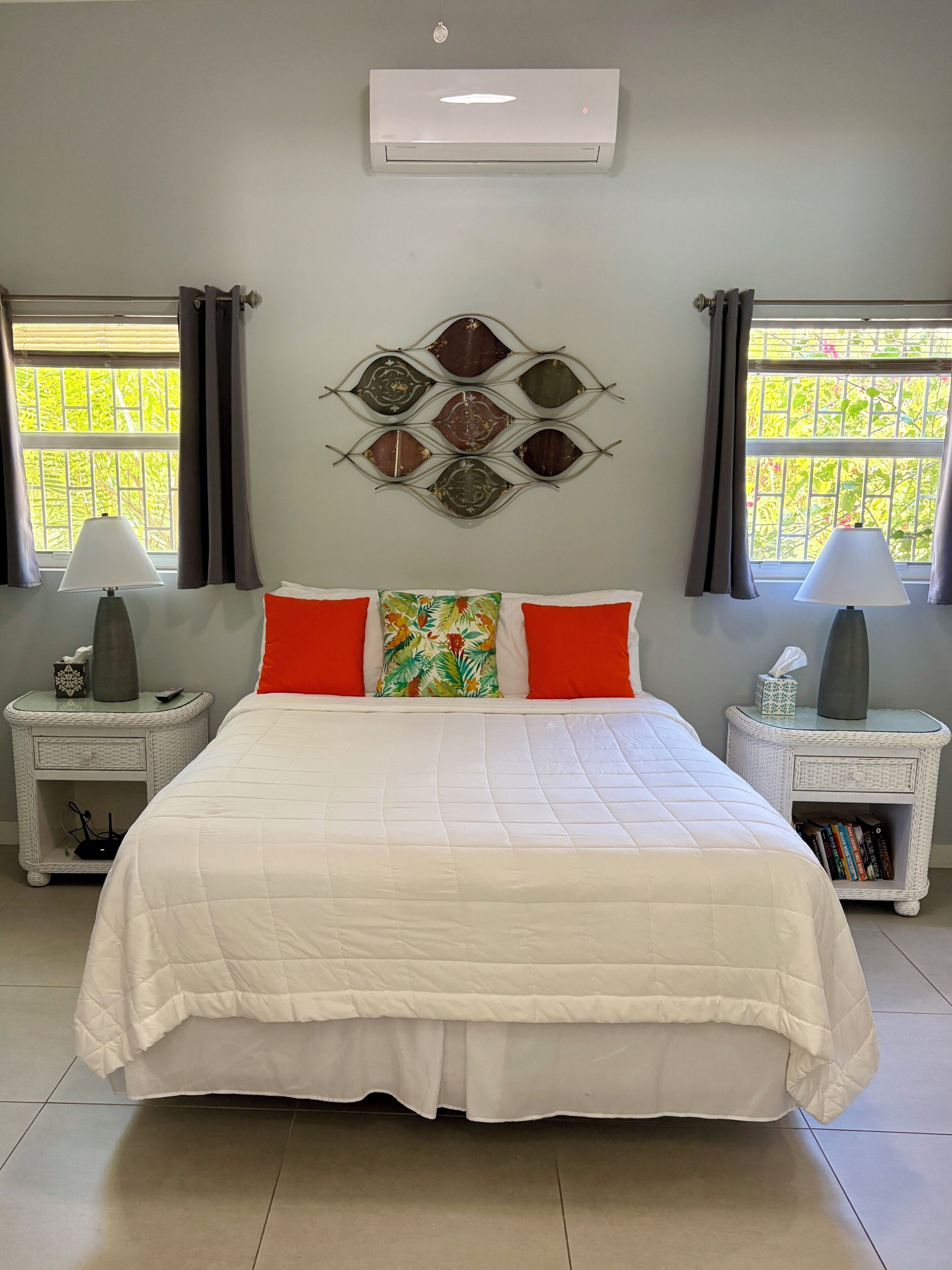 A bedroom with a large bed, two bedside tables, a wall-mounted air conditioner, and a window with curtains.