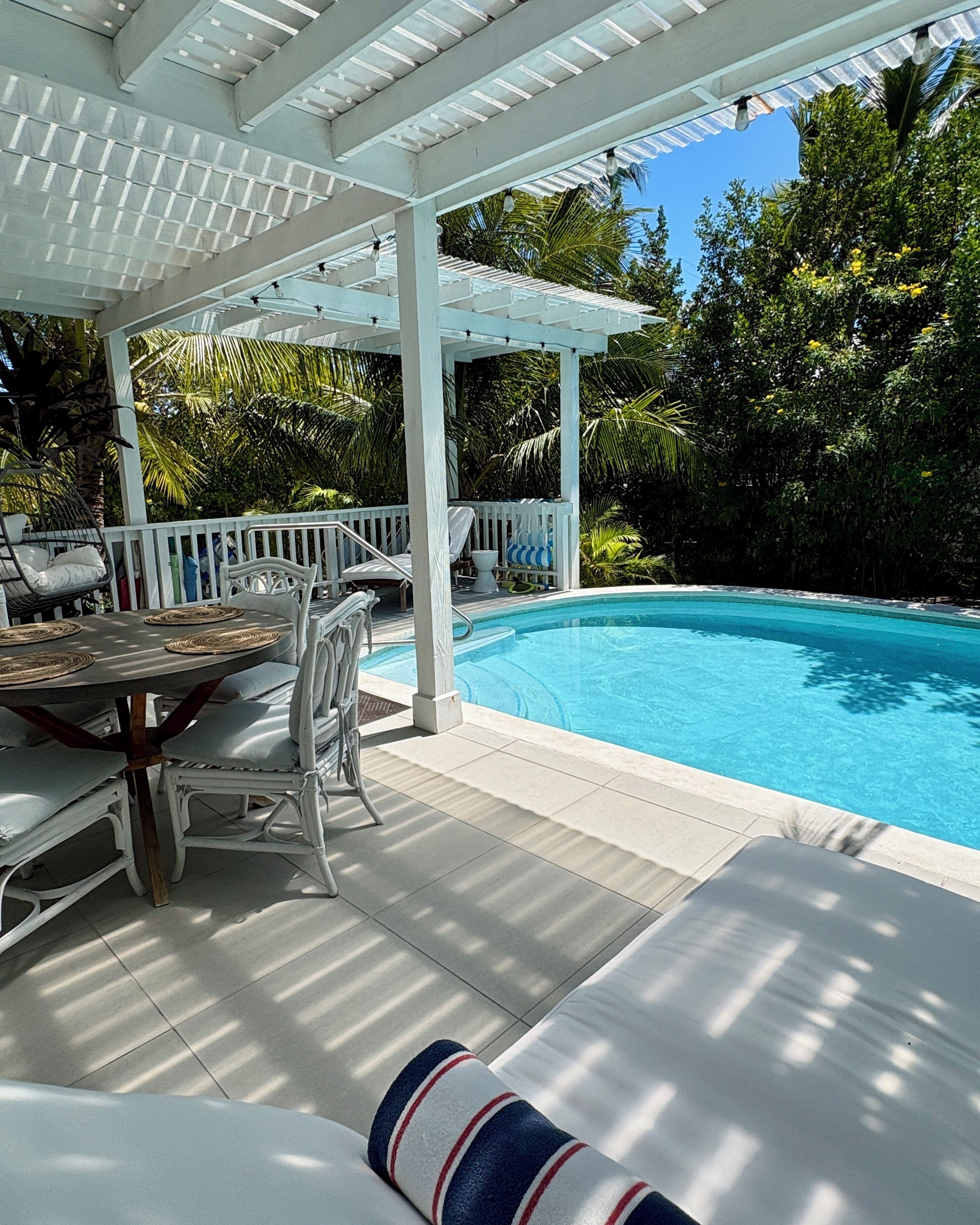 Un espace extérieur abrité, doté d’une piscine, de mobilier blanc et d’une végétation luxuriante.