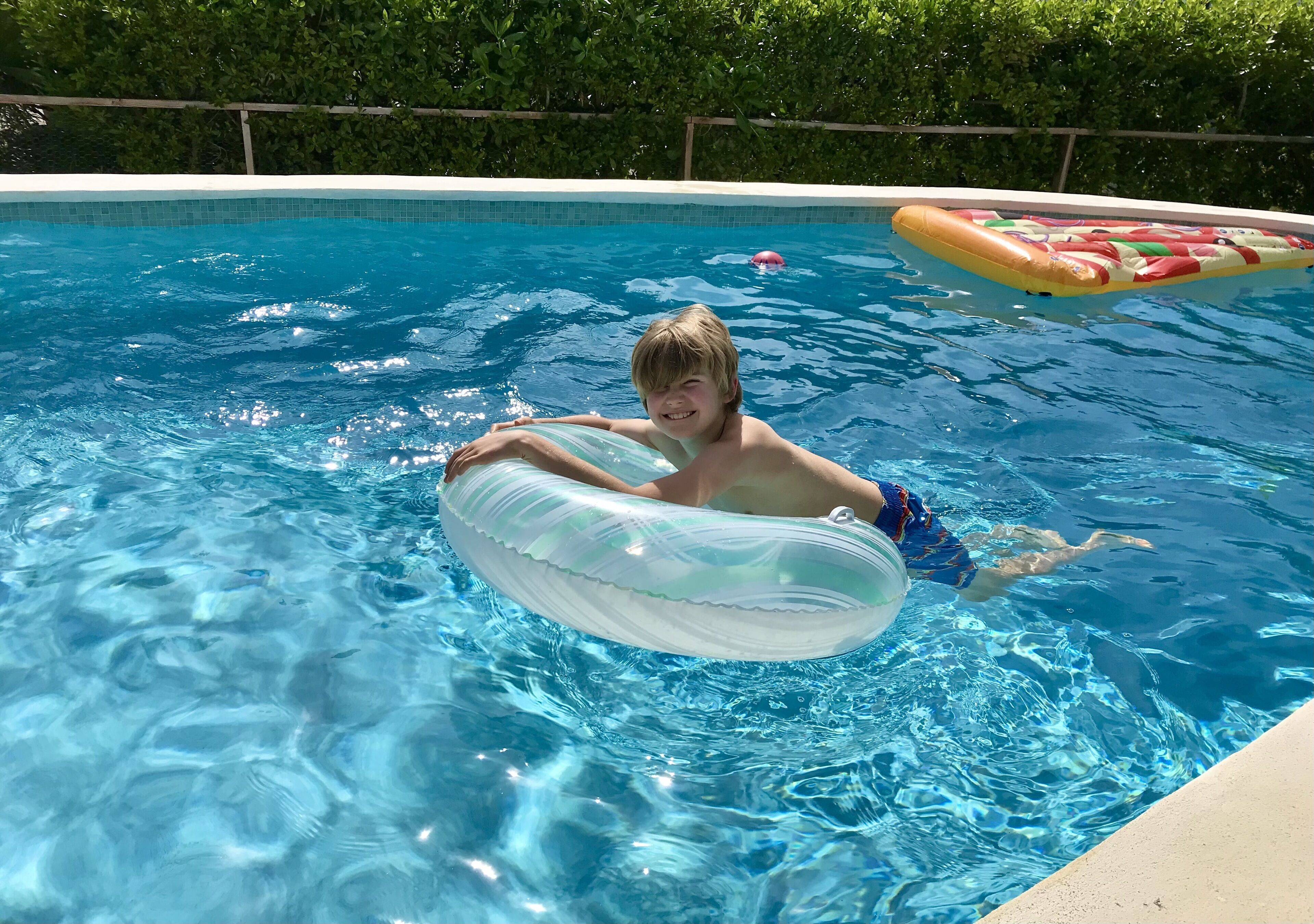 A swimming pool with clear blue water, a person floating on an inflatable ring, and a pool float with a colorful design.