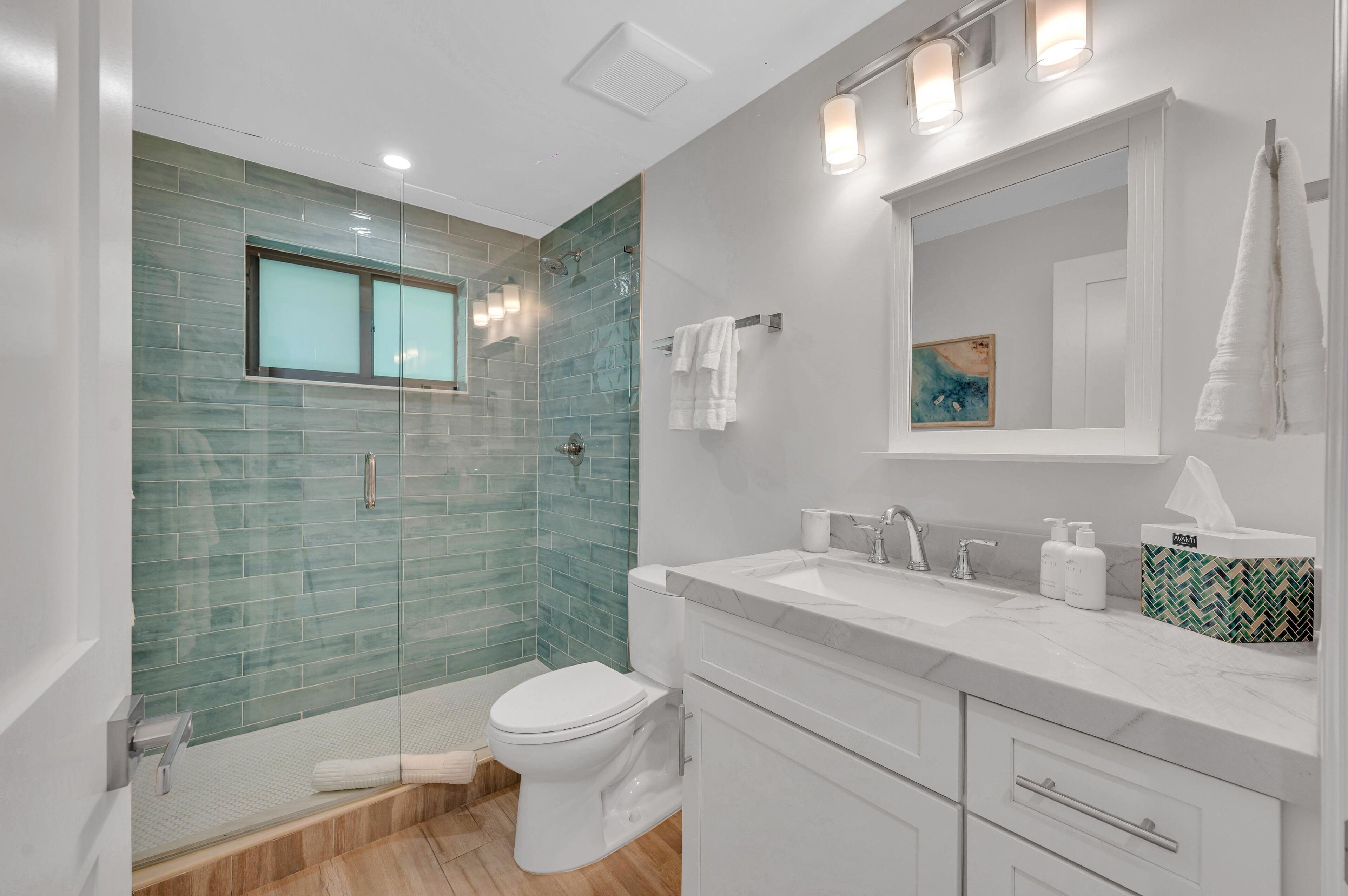A modern bathroom with a glass shower enclosure, a white toilet, and a vanity with a mirror and towel rack.