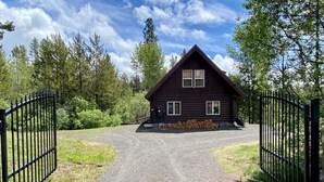 A log cabin with a gravel driveway and black metal gates. - Relaxing 5 Bedroom Log Cabin with Large Backyard (Donnelly)