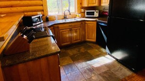 A kitchen with wooden cabinets, a black refrigerator, a microwave, and a sink. - Relaxing 5 Bedroom Log Cabin with Large Backyard (Donnelly)