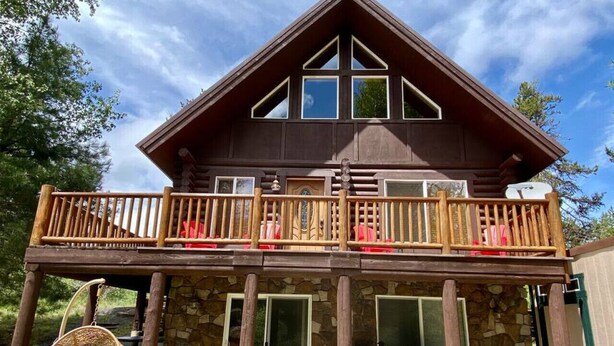 A two-story wooden cabin with a balcony, stone foundation, and large windows. - Relaxing 5 Bedroom Log Cabin with Large Backyard (Donnelly)