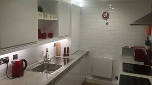A modern kitchen with white cabinets, a stainless steel sink, a red kettle, and a clock on the wall. - Harpenden House Apartment 2 Quality at its Best! (Harpenden)