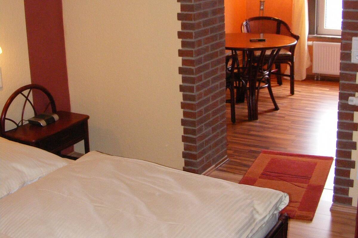 Ein Schlafzimmer mit einem Bett, einem kleinen Tisch mit Stuhl, einem Esstisch mit Stühlen und einer Ziegelstütze.