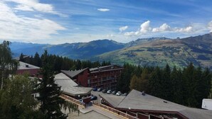 A mountain lodge with multiple floors, a parking area, and a view of surrounding mountains.