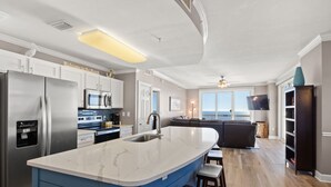 Una cocina moderna con una isla grande, electrodomésticos de acero inoxidable y vistas al área de estar.