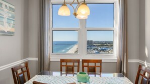Un comedor con una mesa dispuesta para cuatro personas, vista al océano y al muelle, y una araña colgante.