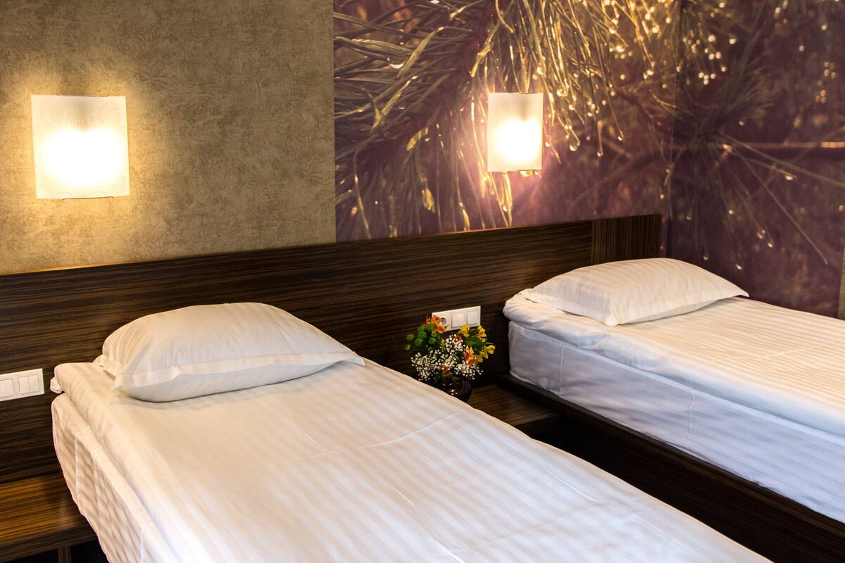 A hotel room with two beds, a nightstand with a vase of flowers, and wall-mounted lights.