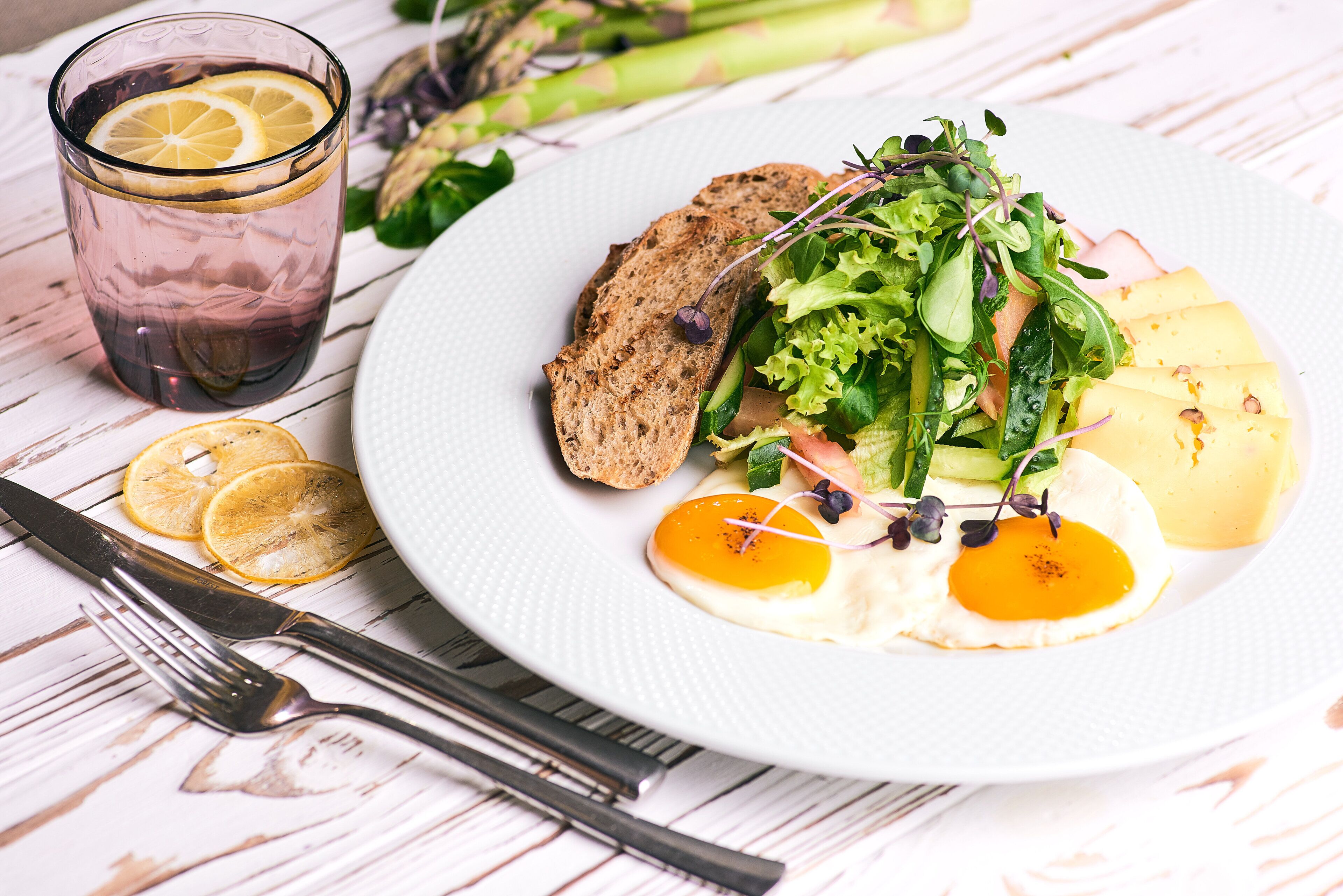 A plate of food with a glass of drink, asparagus, and a fork and knife on a table.