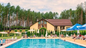 A swimming pool area with lounge chairs and umbrellas, surrounded by tall trees.