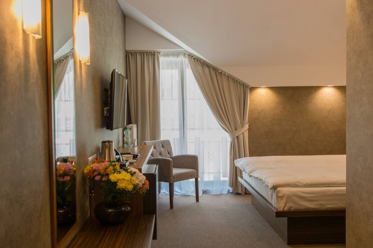 A hotel room with a bed, a desk, a chair, a mirror, and a window with curtains.