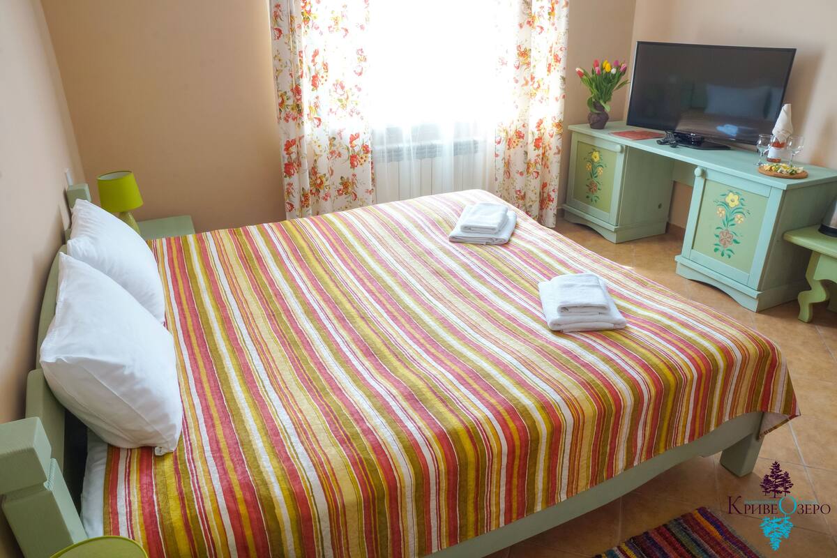 A hotel room with a bed, a television, a desk with a computer, and a window with curtains.