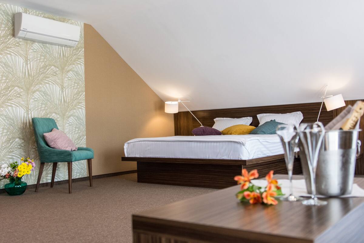 A bedroom with a bed, a chair, a bedside table with a lamp, and a flower arrangement.