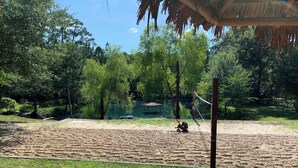 Une zone de plage sablonneuse avec un filet de volley-ball, un banc en bois et une structure dotée d’un toit de chaume.