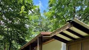 Une structure en bois dotée d’un porche couvert et d’une porte, le tout entouré de verdure.
