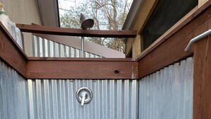 Un escalier en bois mène à un espace extérieur abrité, doté d’une porte en métal, d’un toit en métal et d’une rambarde en bois.