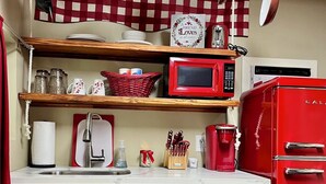Une cuisine avec des meubles en bois, un réfrigérateur rouge, un four à micro-ondes et des casseroles suspendues.
