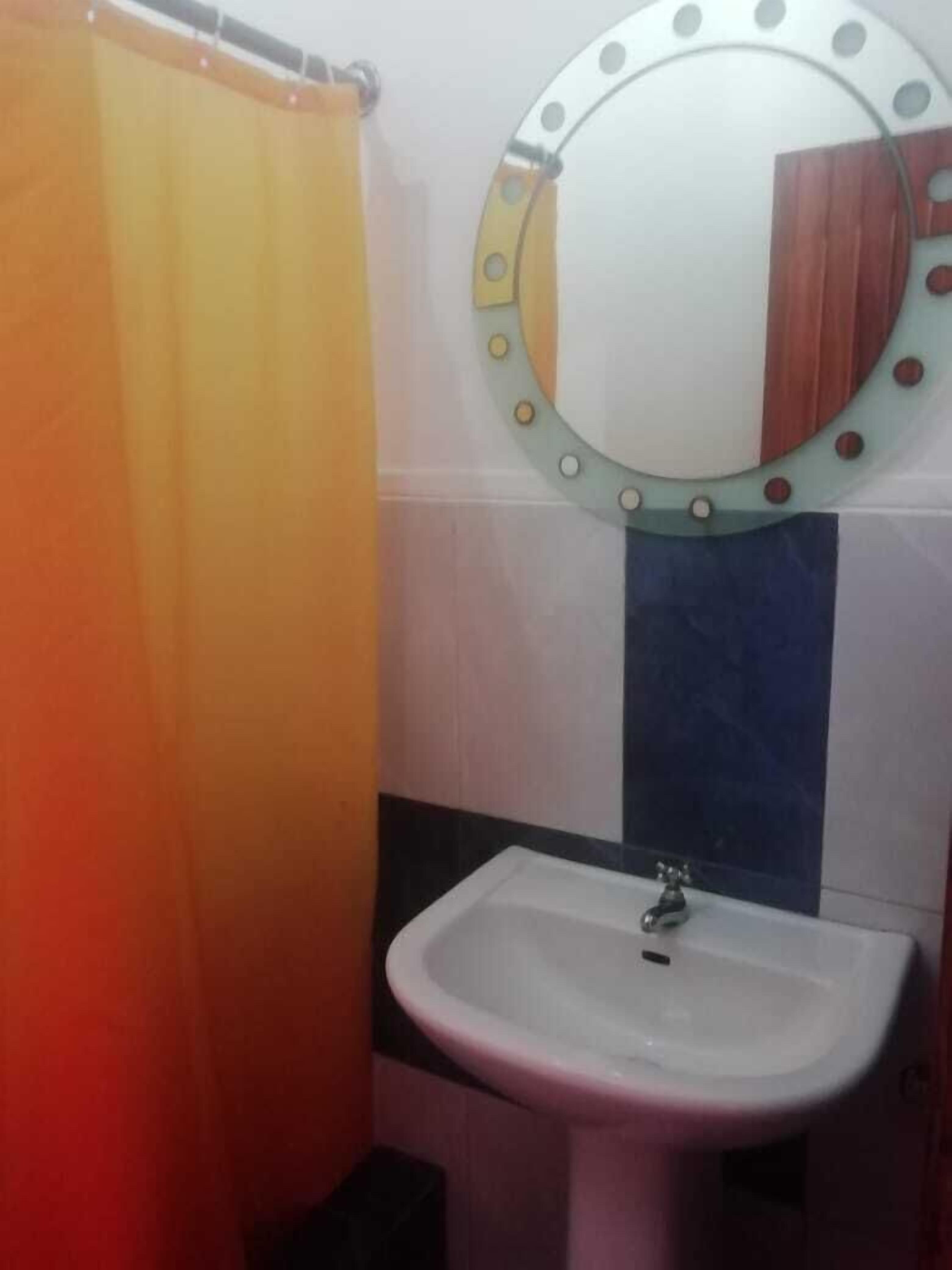 Un baño con un lavabo blanco, un espejo con marco decorativo y una cortina de ducha.
