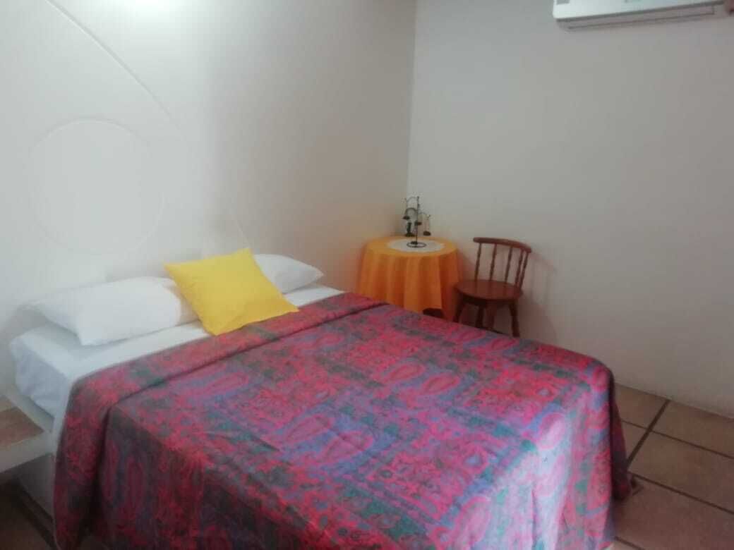 A bedroom with a bed, a small round table with a chair, and a wall-mounted shelf.