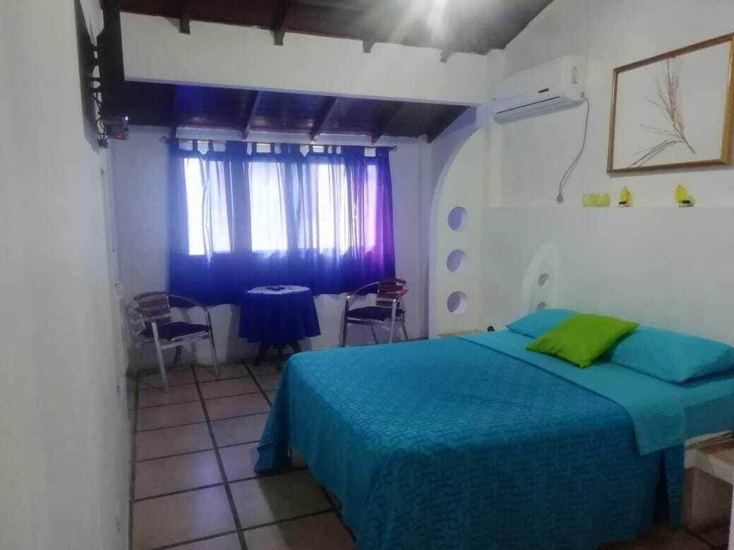 Una habitación con cama, una mesita, sillas y una ventana con cortinas.