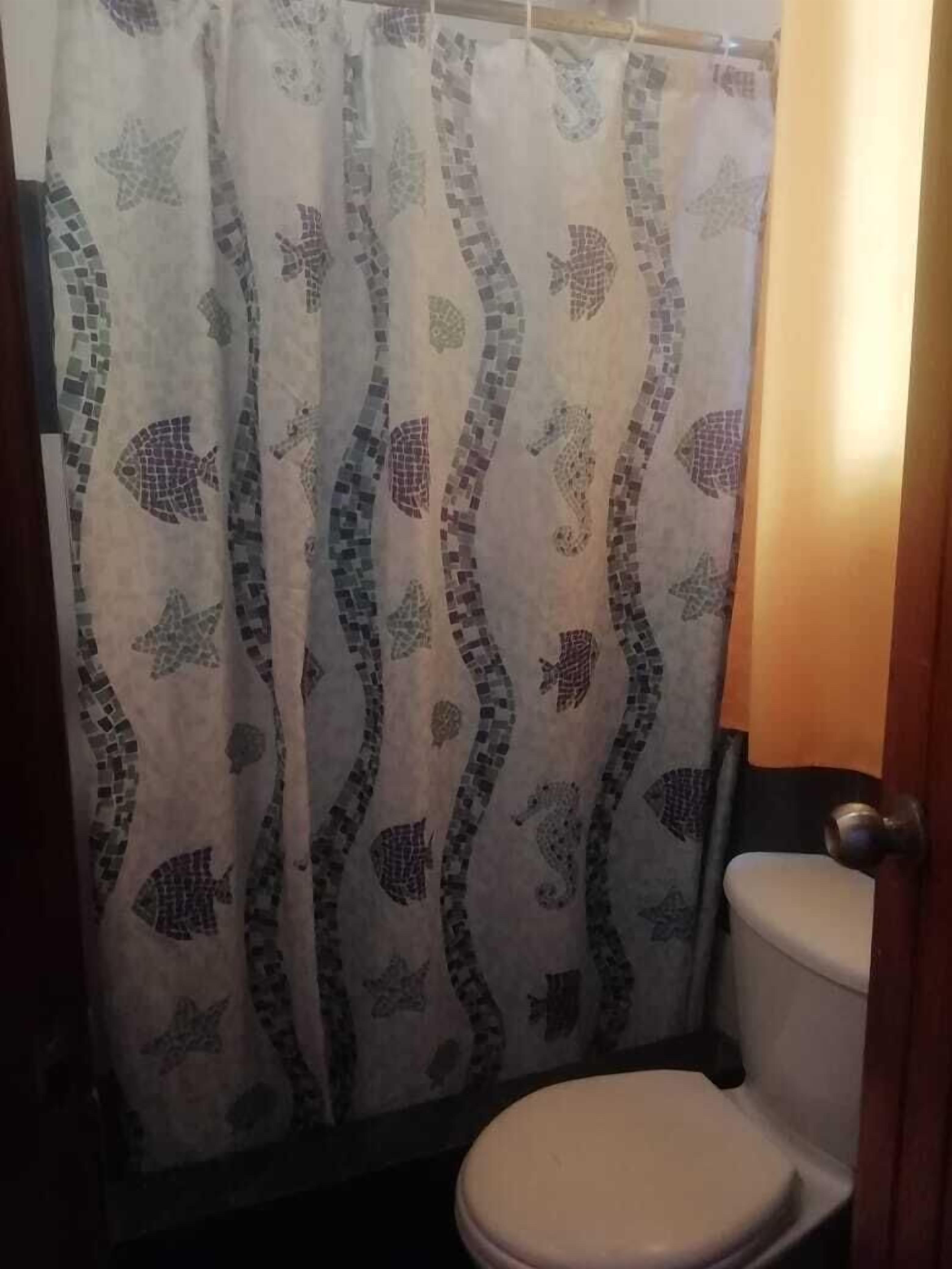 Un baño con inodoro y cortina de ducha con un diseño de mosaico de peces y caballitos de mar.