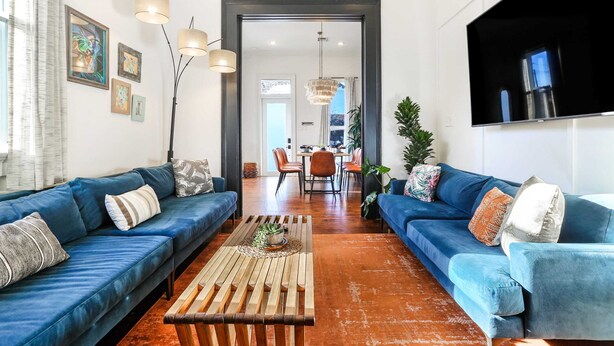 Ein modernes Wohnzimmer mit zwei blauen Sofas, einem Holztisch und einem Essbereich im Hintergrund.