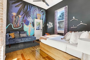 A modern bedroom with a mural, a sofa, a bed, a window, and a ceiling fan.