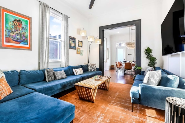 A modern living room with blue sofas, wooden coffee tables, and a large painting on the wall.