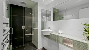 Een moderne badkamer met een douchecabine van glas, een witte wastafel en een badmeubel met groene tegels.