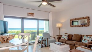 Un salon avec vue sur la plage, doté d’un ventilateur de plafond, d’un téléviseur et d’un coin salon confortable.