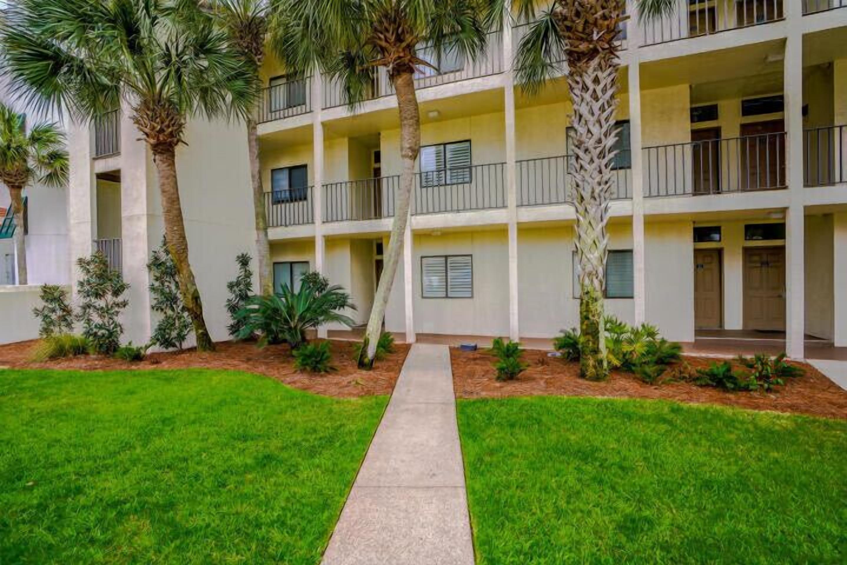 A multi-story hotel with a central courtyard, palm trees, and a concrete pathway.