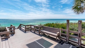 Une terrasse en bois, dotée de bancs, qui offre une vue sur une plage aux eaux turquoise et cristallines.