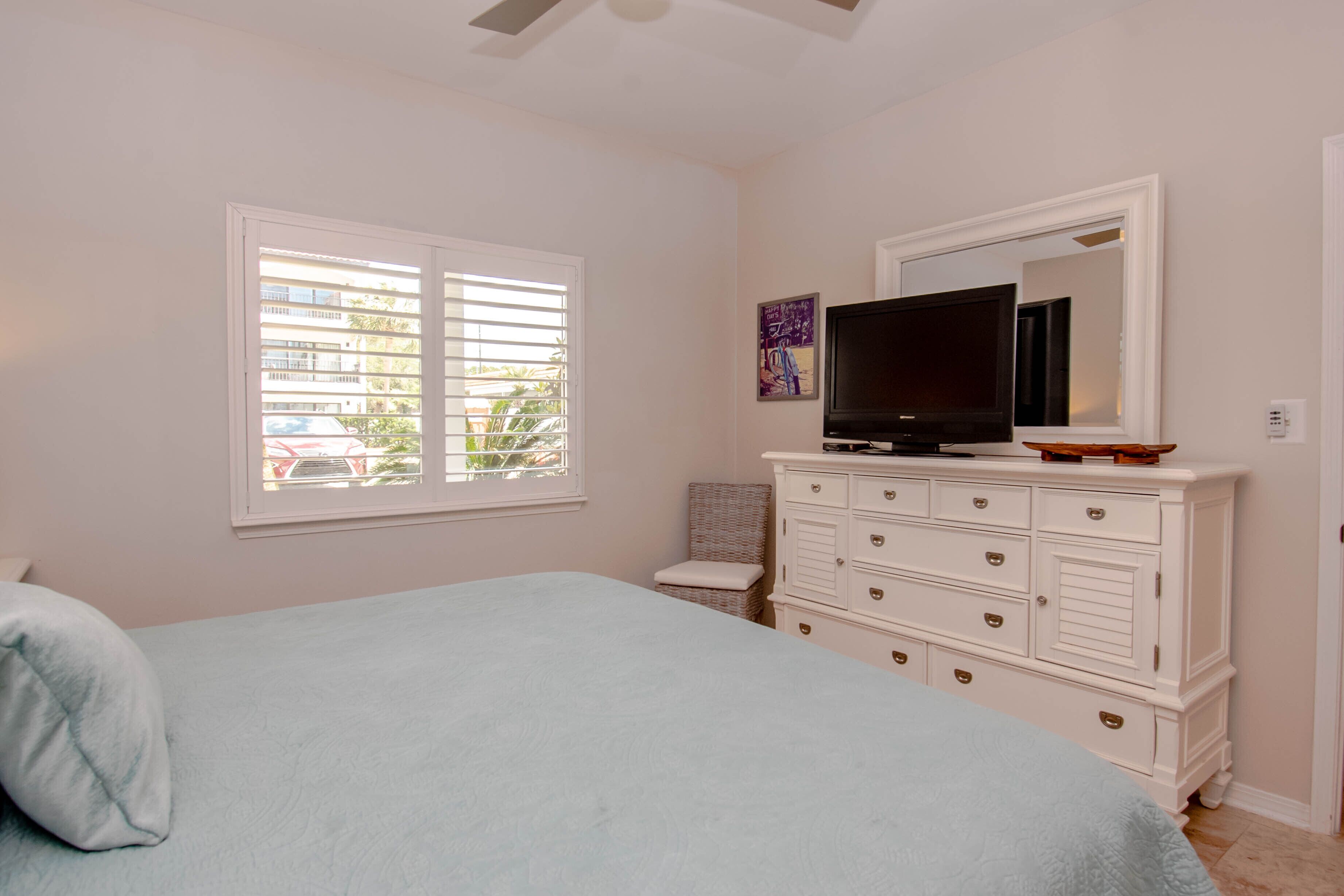 Un dormitorio con una cama, un tocador, un televisor y una ventana con persianas.