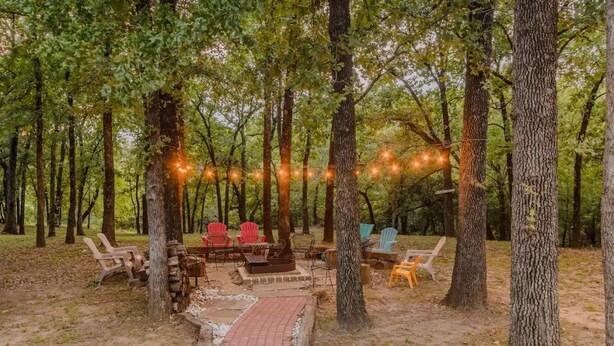 Een terras met stoelen en een vuurkorf, omringd door bomen en sfeerverlichting.