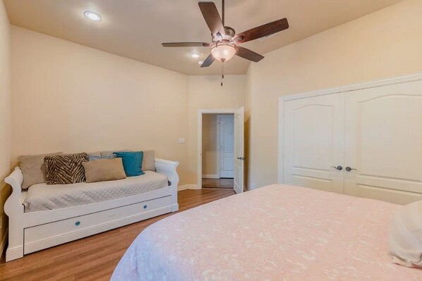A bedroom with a bed, a white sofa with cushions, a ceiling fan, and a door.