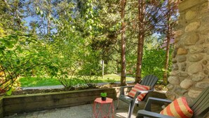 Eine Terrasse mit zwei Stühlen und einem kleinen Tisch, umgeben von Grünpflanzen und einer Steinmauer.