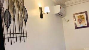 Uma área de refeições com uma mesa de mármore preto e cadeiras brancas, um ar-condicionado fixado na parede e arte decorativa.