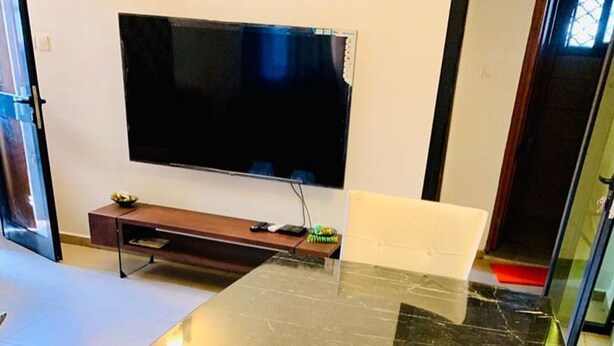 Quarto com bancada de mármore grande, TV de tela plana na parede e pequena mesa de madeira com uma planta.