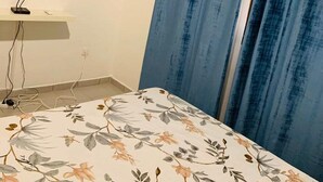 Quarto com cama, televisão na parede e cortinas azuis.