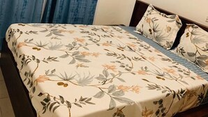 Quarto com cama, colcha florida e janela com cortinas azuis.